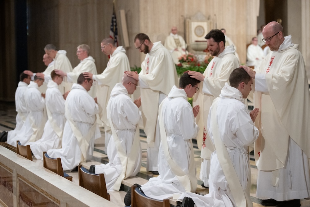 Dominican priests lay hands on a newly ordained friar during the ordination rite, signifying blessing and participation in the priesthood of Christ